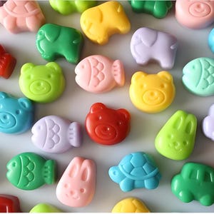 Pode incluir: Conjunto de sabonetes artesanais coloridos em forma de animais e veículos. Os sabonetes são de várias cores, incluindo vermelho, azul, verde, amarelo e roxo.