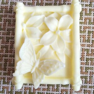 May include: A white soap bar with a raised design of a butterfly and flowers in a bamboo frame.