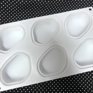 Puede incluir: Molde de silicona blanco con seis cavidades de forma irregular. El molde est&aacute; dise&ntilde;ado para hacer peque&ntilde;os pasteles u otros postres.