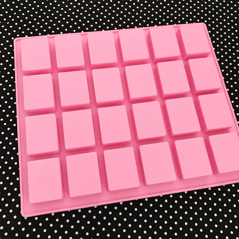 K&ouml;nnte beinhalten: Eine rosa Silikonform mit einem Raster aus 28 rechteckigen Hohlr&auml;umen. Die Form ist f&uuml;r die Herstellung kleiner, quadratischer Gegenst&auml;nde konzipiert. Der Hintergrund ist ein schwarz-wei&szlig;es Polka-Dot-Muster.