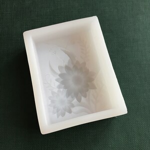 Puede incluir: Molde de silicona blanco con un dise&ntilde;o floral. El molde presenta dos flores grandes con detalles intrincados y hojas.