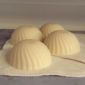 以下が含まれることがあります： 白い丸いドーム型の石鹸が4つ、白い布の上に置かれています。石鹸には渦巻き模様があります。