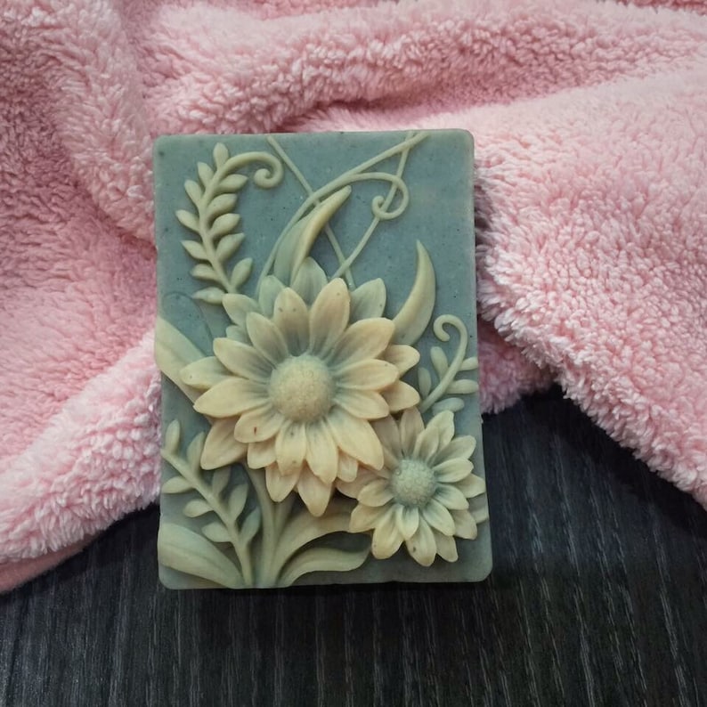 Puede incluir: Una pastilla de jab&oacute;n hecha a mano con un dise&ntilde;o floral. El jab&oacute;n es de color azul claro con un patr&oacute;n floral blanco. El jab&oacute;n est&aacute; sobre una toalla rosa.