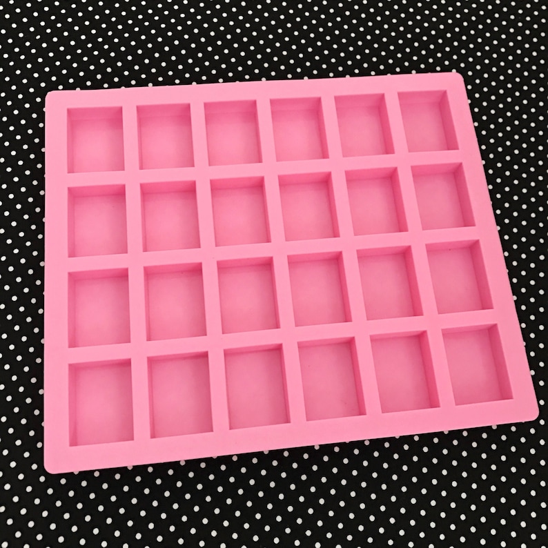 K&ouml;nnte beinhalten: Eine rosa Silikonform mit 30 rechteckigen Hohlr&auml;umen. Die Form dient zur Herstellung kleiner, quadratischer Gegenst&auml;nde wie Seifen, Kerzen oder Pralinen. Der Hintergrund ist ein schwarz-wei&szlig;es Polka-Dot-Muster.