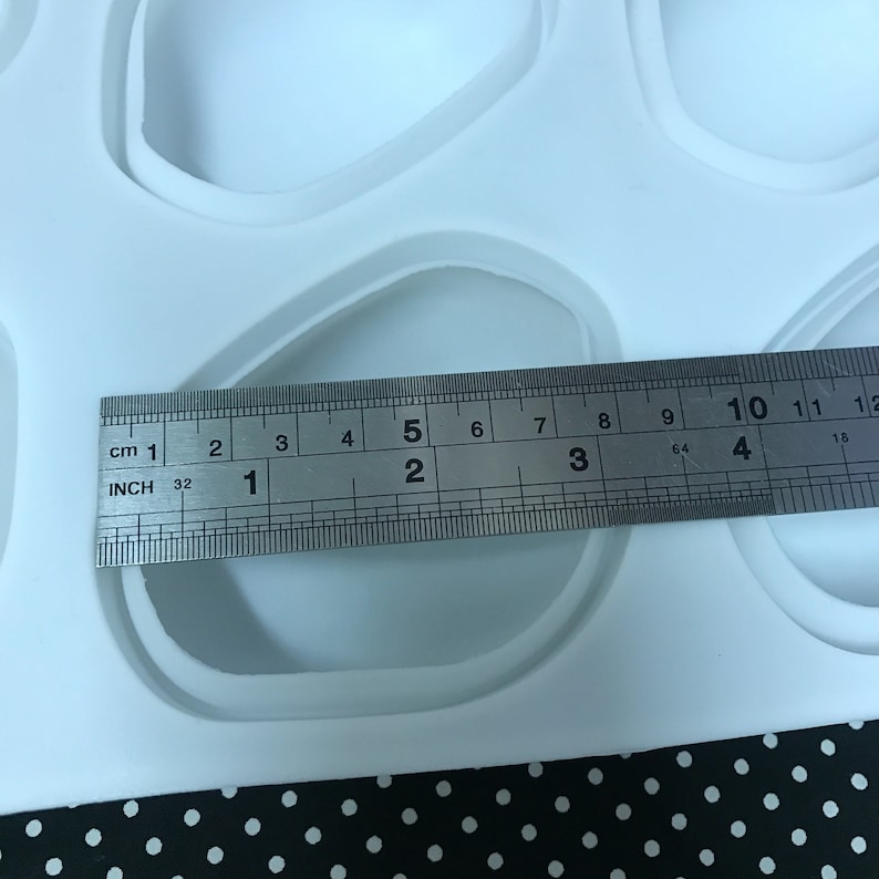 Puede incluir: Un molde de silicona blanco con m&uacute;ltiples cavidades de forma ovalada. Una regla se coloca encima del molde, mostrando que el tama&ntilde;o de las cavidades es de aproximadamente 5 cm de largo.