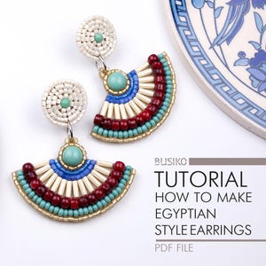 Op de afbeelding: Een paar handgemaakte oorbellen in Egyptische stijl. De oorbellen hebben een waaierontwerp met turquoise, rode, blauwe en crèmekleurige kralen. Ze hebben een cirkelvormige bovenkant met een turquoise kraal in het midden en een goudkleurige metalen haak.