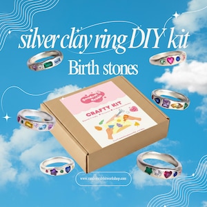 May include: A silver clay ring DIY kit featuring a brown cardboard box with a label that reads Random Rabbit Crafty Kit. Six silver rings with various colourful, multi-shaped gemstones are arranged around the box against a blue sky background.