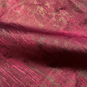 May include: Burgundy fabric with a gold metallic pattern. The fabric has a subtle sheen and a textured surface.