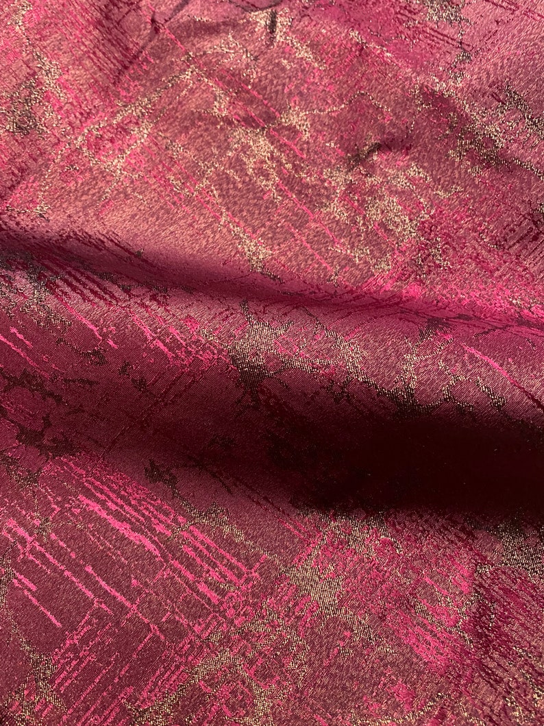 May include: Burgundy fabric with a gold metallic pattern. The fabric has a subtle sheen and a textured surface.