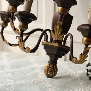 May include: A dark brown wooden chandelier with gold accents and five candle holders. The chandelier has a traditional design with ornate details.