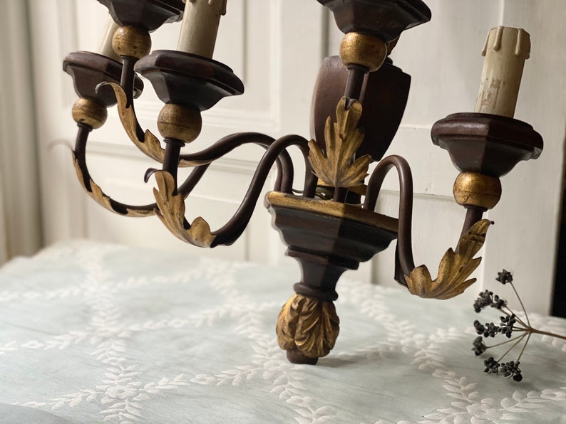 May include: A dark brown wooden chandelier with gold accents and five candle holders. The chandelier has a traditional design with ornate details.