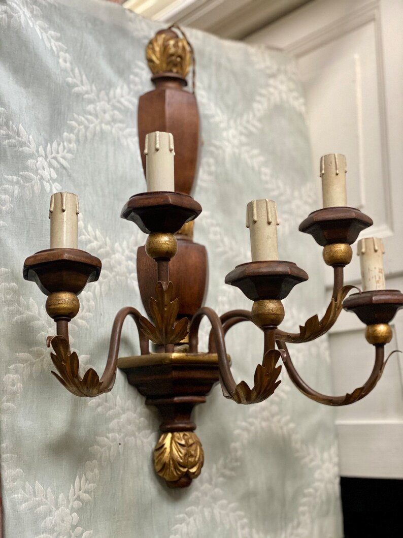 May include: A wooden wall sconce with five candle-style light bulbs. The sconce has a gold leaf finish and ornate details.