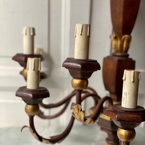 May include: A wooden wall sconce chandelier with five candle holders. The chandelier is painted brown with gold accents. The candle holders are made of wood and have a gold finish. The chandelier is a vintage style and would be a great addition to any home.