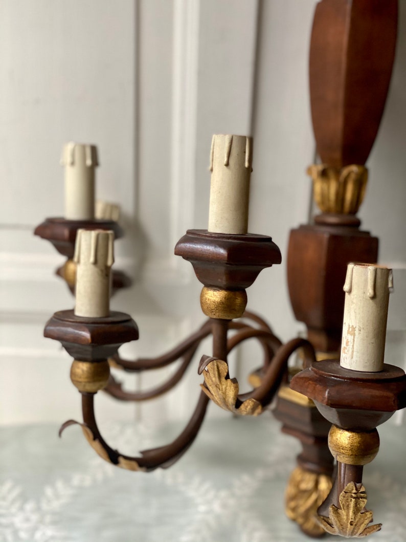 May include: A wooden wall sconce chandelier with five candle holders. The chandelier is painted brown with gold accents. The candle holders are made of wood and have a gold finish. The chandelier is a vintage style and would be a great addition to any home.