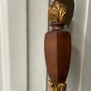 May include: A wooden finial with a gold leaf design. The finial is a decorative element often used on furniture.