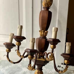 May include: A wooden wall sconce chandelier with six light bulbs and gold accents. The chandelier has a dark brown finish and features ornate carvings.