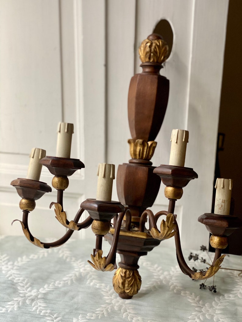 May include: A wooden wall sconce chandelier with six light bulbs and gold accents. The chandelier has a dark brown finish and features ornate carvings.