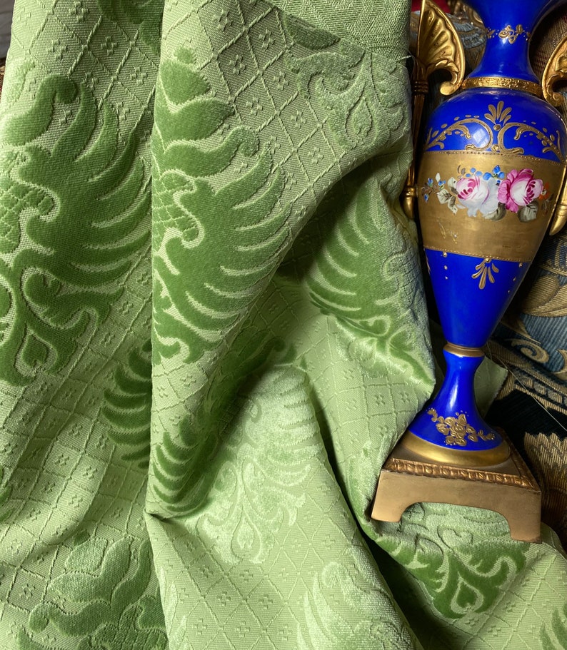 May include: A green velvet fabric with a damask pattern. The fabric is draped over a blue and gold decorative vase with floral details.