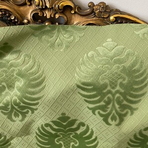 May include: Green velvet fabric with a damask pattern featuring stylized eagle motifs. The fabric has a subtle sheen and a textured surface.