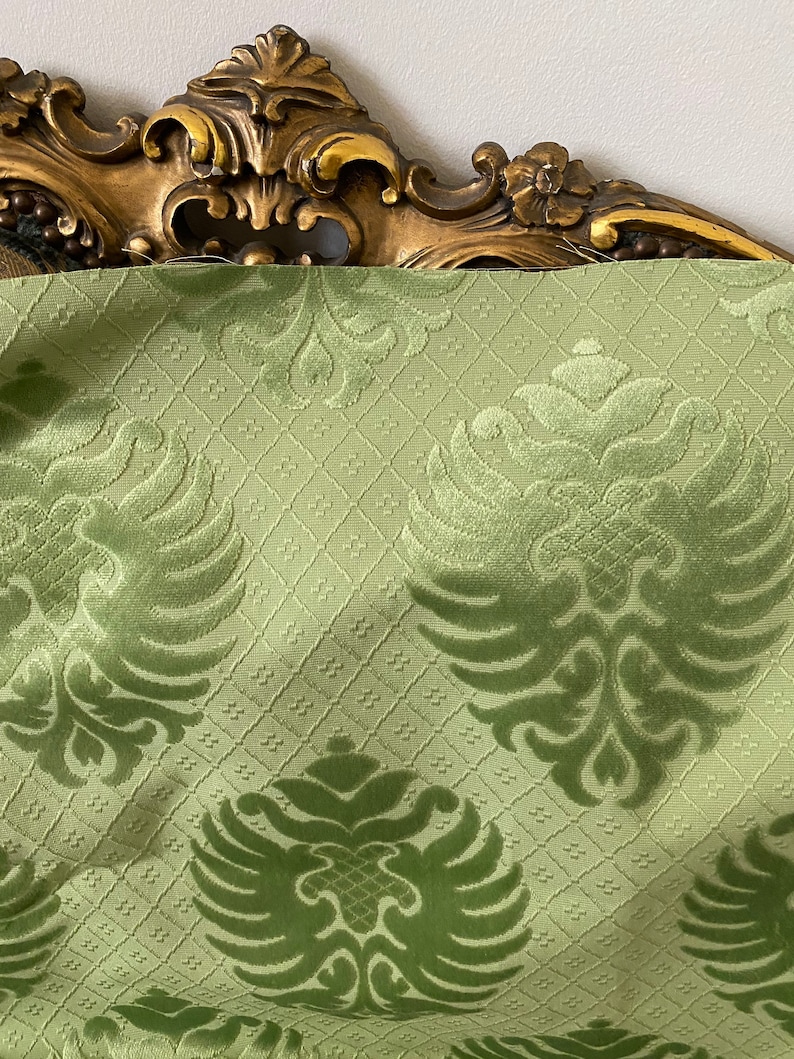 May include: Green velvet fabric with a damask pattern featuring stylized eagle motifs. The fabric has a subtle sheen and a textured surface.