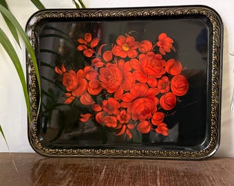 May include: Rectangular black serving tray with a floral design. The tray features a vibrant red flower bouquet with green leaves. The border has a gold filigree design. A decorative piece for serving.
