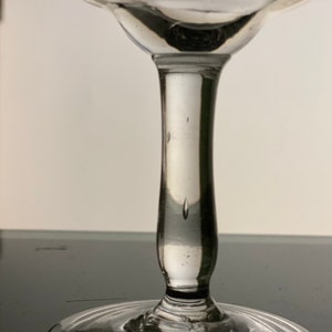 Pu&ograve; includere: Un bicchiere trasparente con stelo, con una coppa arrotondata e un gambo sottile. Il bicchiere ha un design delicato ed elegante, con un bordo svasato e una superficie liscia e lucida. Il bicchiere viene probabilmente utilizzato per servire bevande.