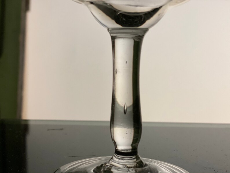 Pu&ograve; includere: Un bicchiere trasparente con stelo, con una coppa arrotondata e un gambo sottile. Il bicchiere ha un design delicato ed elegante, con un bordo svasato e una superficie liscia e lucida. Il bicchiere viene probabilmente utilizzato per servire bevande.