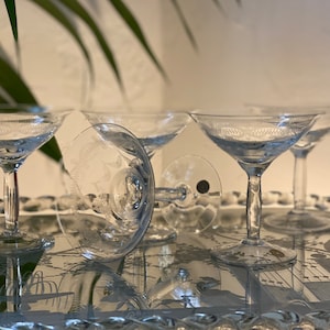 Könnte beinhalten: Vier klare Champagnergläser mit geätzten Designs auf einer verspiegelten Oberfläche.