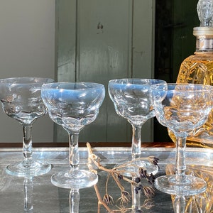 Pu&ograve; includere: Una collezione di bicchieri di cristallo vintage, tra cui quattro calici e una caraffa decorativa. I bicchieri hanno un bordo smerlato e sono su un vassoio d'argento. La caraffa &egrave; color ambra.