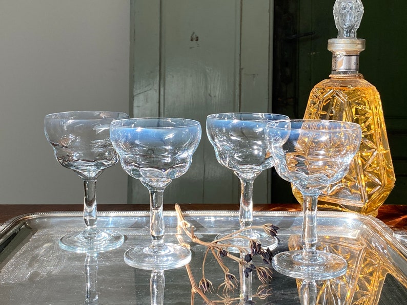 Pu&ograve; includere: Una collezione di bicchieri di cristallo vintage, tra cui quattro calici e una caraffa decorativa. I bicchieri hanno un bordo smerlato e sono su un vassoio d'argento. La caraffa &egrave; color ambra.