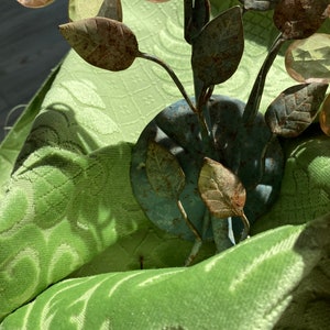May include: A metal flower sculpture with rust-colored leaves and clear glass flowers. The sculpture is sitting on a green fabric surface.
