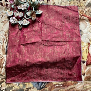May include: A burgundy throw pillow with a subtle gold pattern. The pillow is made of a textured fabric and has a decorative border.
