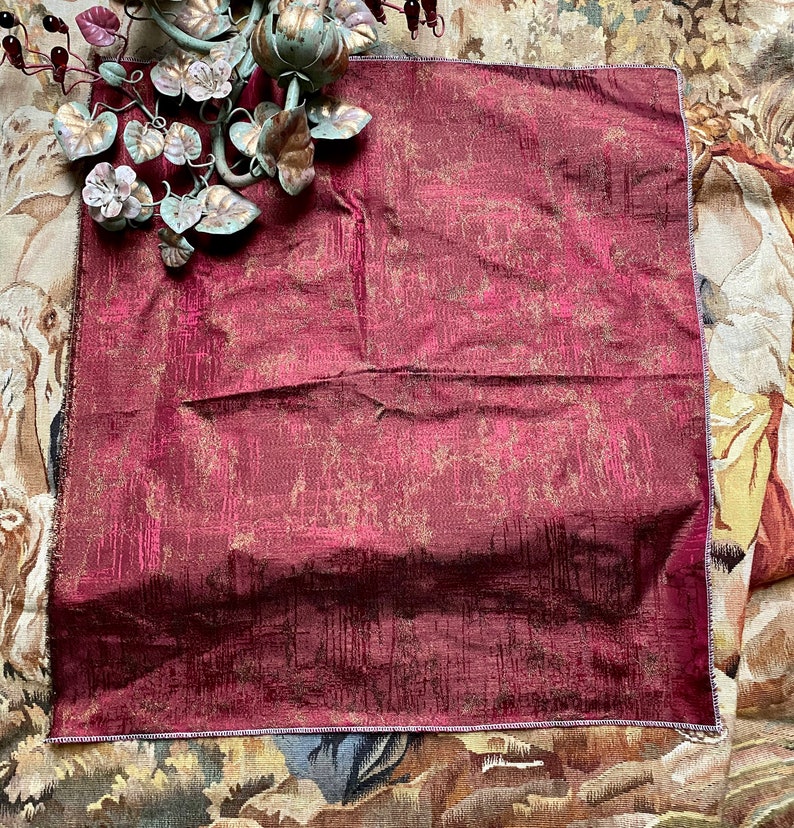 May include: A burgundy throw pillow with a subtle gold pattern. The pillow is made of a textured fabric and has a decorative border.