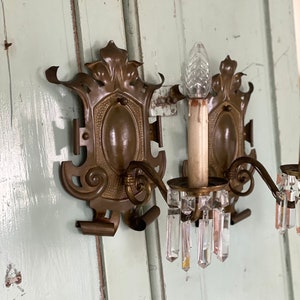 May include: A pair of antique brass wall sconces with crystal prisms. The sconces have a decorative floral design and are in good condition.