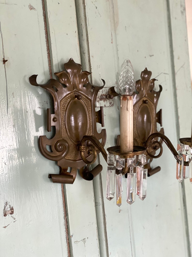 May include: A pair of antique brass wall sconces with crystal prisms. The sconces have a decorative floral design and are in good condition.