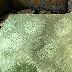 May include: A close-up of a light green fabric with a repeating pattern of stylized double-headed eagles. The fabric has a subtle grid pattern.