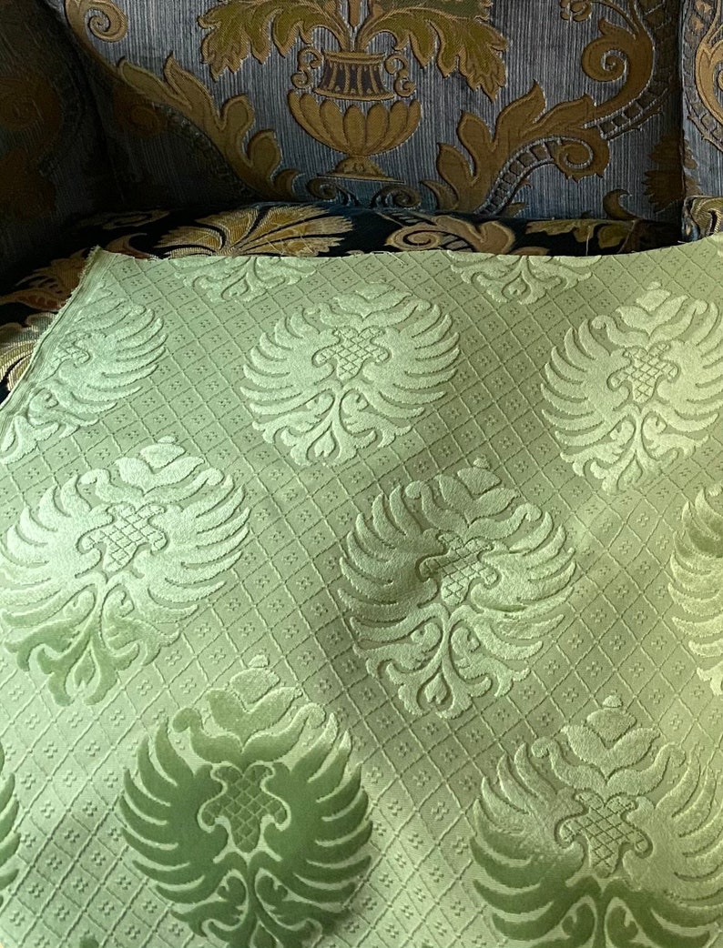 May include: A close-up of a light green fabric with a repeating pattern of stylized double-headed eagles. The fabric has a subtle grid pattern.