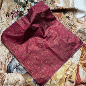 May include: A burgundy and gold fabric swatch with a subtle sheen. The fabric has a textured, woven appearance.