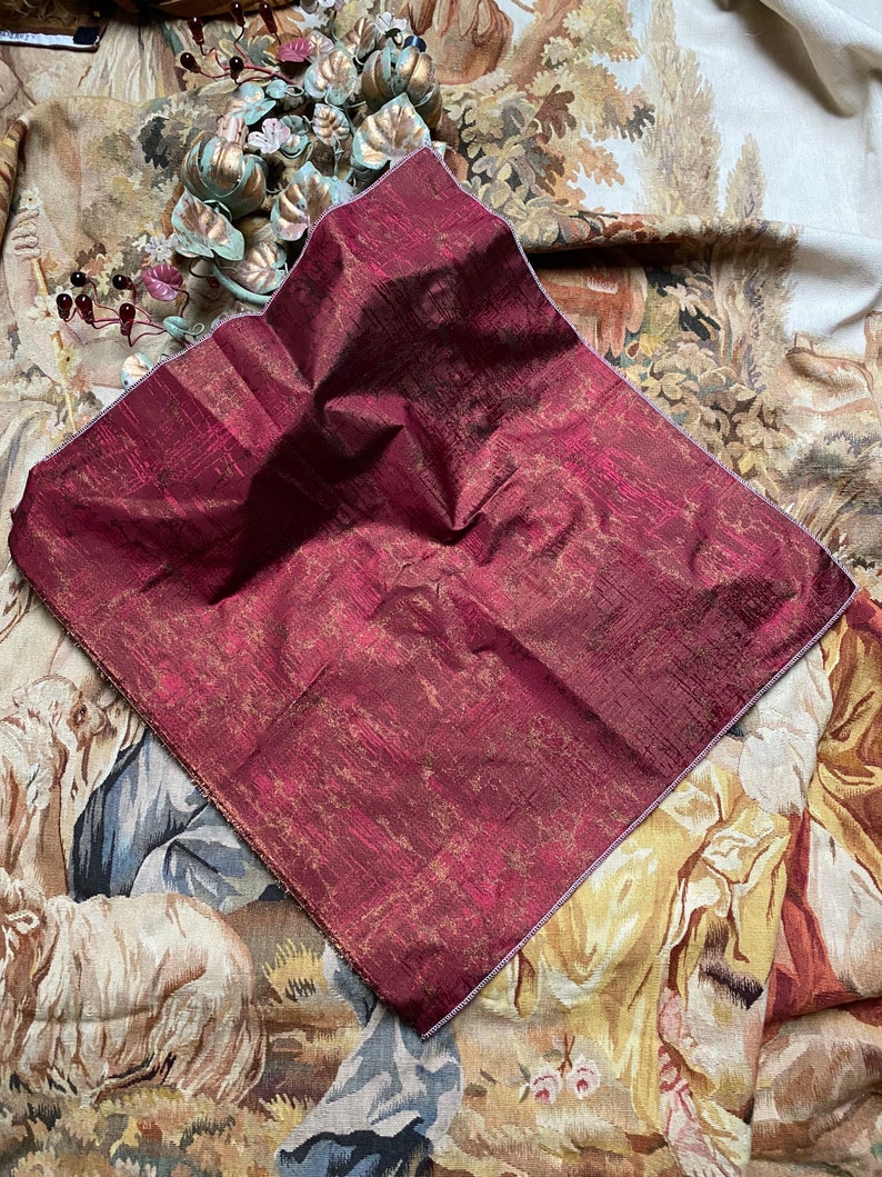 May include: A burgundy and gold fabric swatch with a subtle sheen. The fabric has a textured, woven appearance.