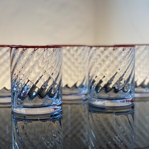 May include: Set of five clear glass tumblers with a red rim and a swirling, textured design.