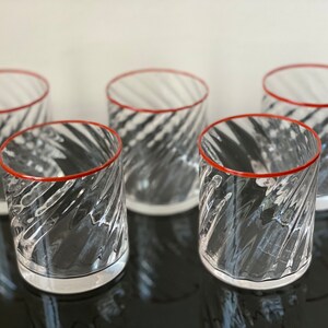 May include: Set of five clear glass tumblers with a red rim and a swirling pattern.