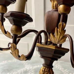 May include: A wooden wall sconce with gold accents and a black metal frame. The sconce has four candle holders and features ornate leaf details.