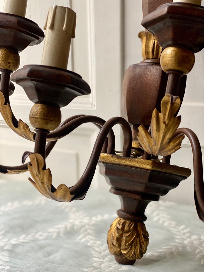 May include: A wooden wall sconce with gold accents and a black metal frame. The sconce has four candle holders and features ornate leaf details.