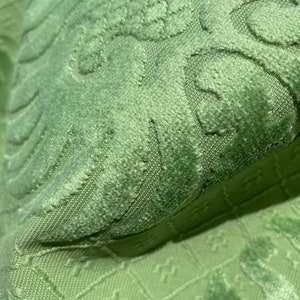 May include: Close-up of a green fabric with a textured, embossed pattern. The fabric has a soft, velvety feel.