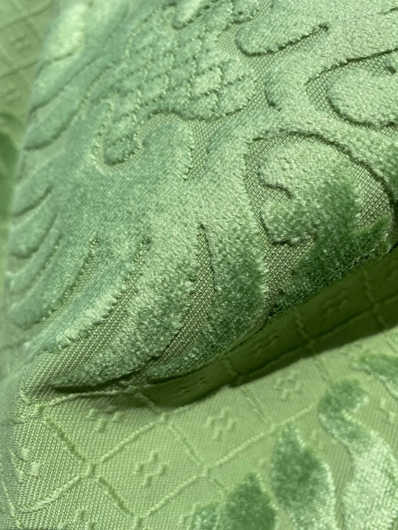 May include: Close-up of a green fabric with a textured, embossed pattern. The fabric has a soft, velvety feel.
