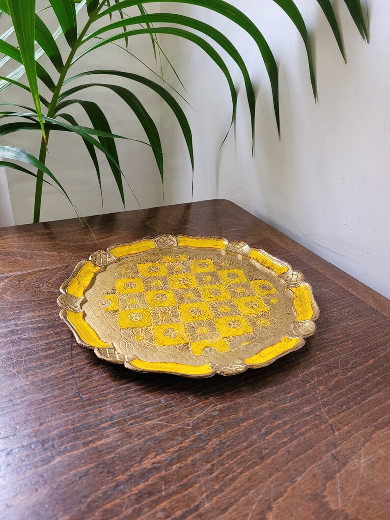Op de afbeelding: Een ronde, gouden dienblad met een gele rand en een ingewikkeld, gegraveerd ontwerp. Het dienblad ligt op een houten oppervlak.