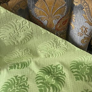 May include: Close-up of a green fabric with a damask pattern. The fabric has a raised texture and a subtle sheen. The fabric is perfect for upholstery or drapery.