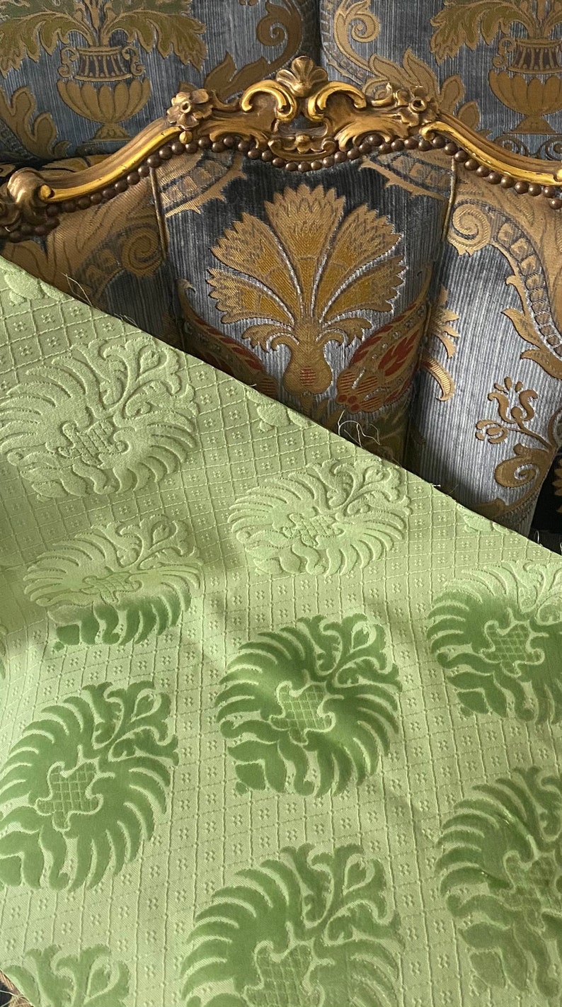 May include: Close-up of a green fabric with a damask pattern. The fabric has a raised texture and a subtle sheen. The fabric is perfect for upholstery or drapery.