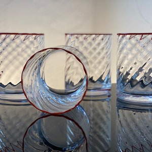 May include: Four clear glass tumblers with a red rim and a swirling, textured design. The tumblers are stacked on top of each other.