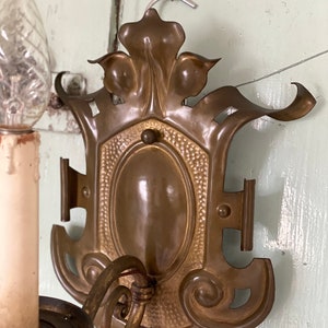 May include: A vintage brass wall sconce with an ornate design. The sconce features a single candle holder and a decorative backplate with a floral motif.